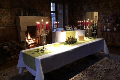 Château en briques rouges entouré de pelouses et d'arbres, sous un ciel clair et ensoleillé.