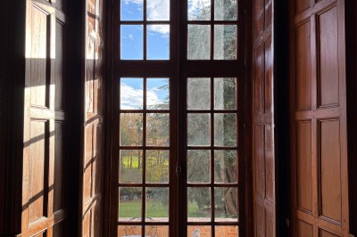 Château en briques rouges entouré de pelouses et d'arbres, sous un ciel clair et ensoleillé.