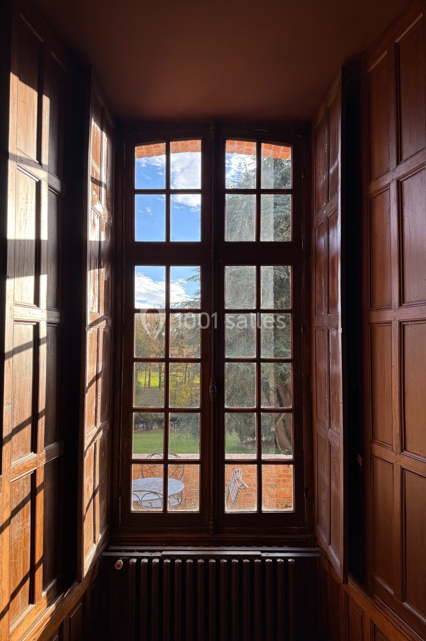 Fenêtre en bois à carreaux laissant entrer la lumière, avec vue sur un jardin et une table extérieure.