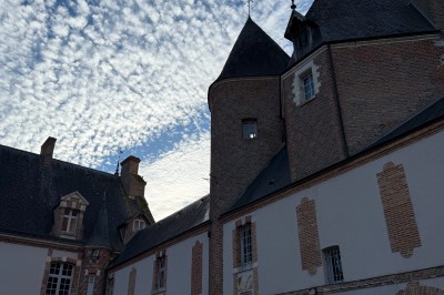 Château en briques rouges entouré de pelouses et d'arbres, sous un ciel clair et ensoleillé.