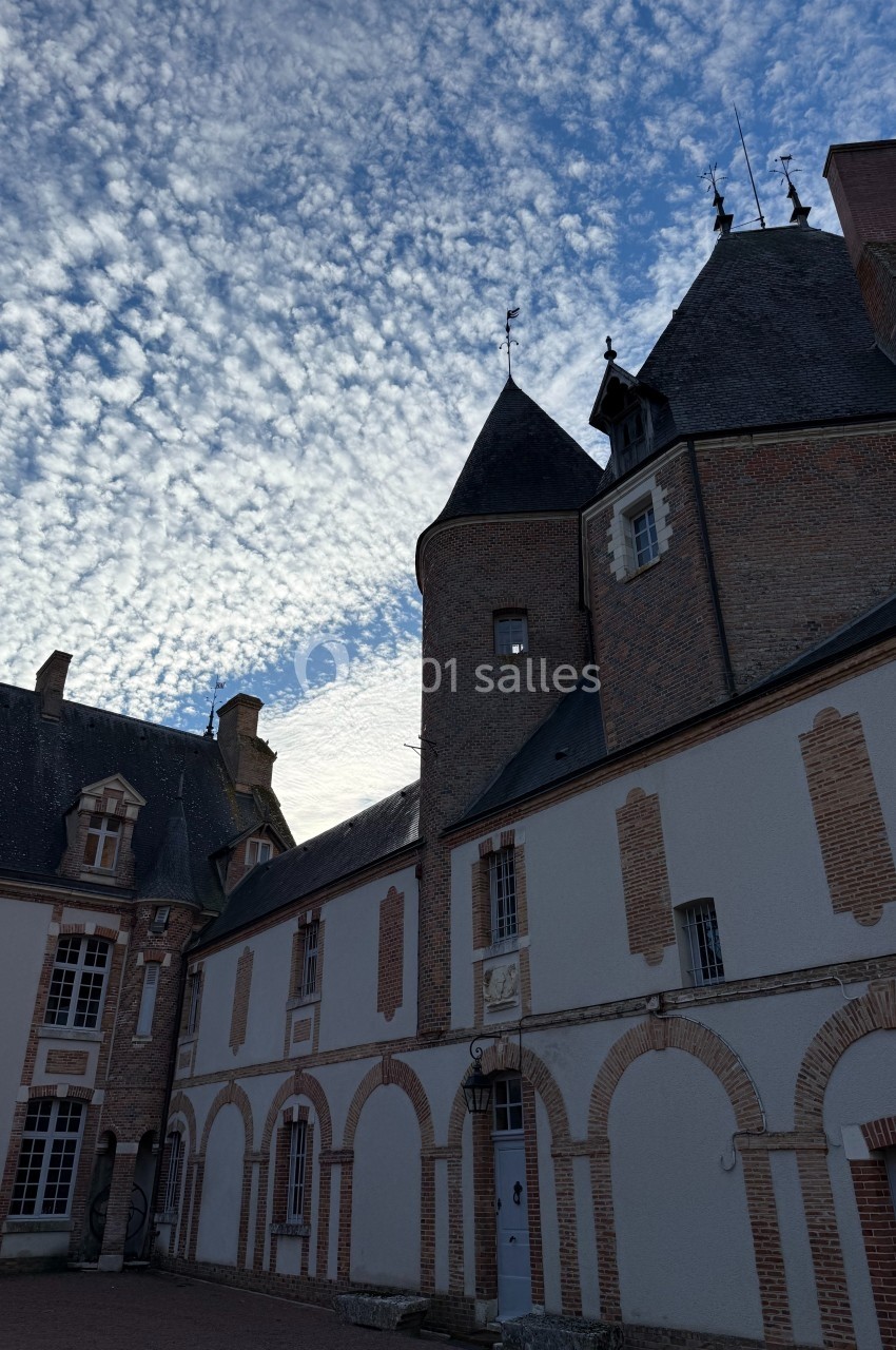 Façade d'un bâtiment historique en briques et pierres sous un ciel partiellement couvert de nuages.