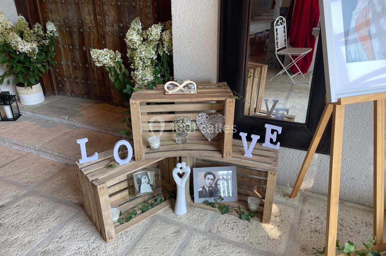 Décoration romantique avec caisses en bois, cadres photo, lettres ’LOVE’, fleurs blanches et objets décoratifs.