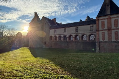 Château en briques rouges entouré de pelouses et d'arbres, sous un ciel clair et ensoleillé.