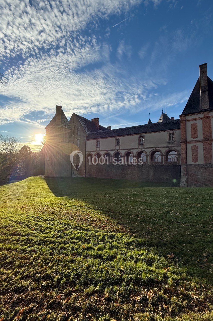 Vue d'un bâtiment historique en pierre et briques au coucher du soleil, entouré d'une pelouse et d'arbres.