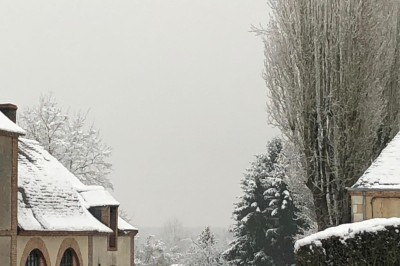 Château en briques rouges entouré de pelouses et d'arbres, sous un ciel clair et ensoleillé.