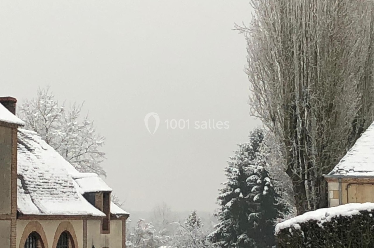 Paysage hivernal avec des bâtiments aux toits enneigés, des arbres givrés et un ciel gris clair.