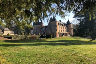 Château en briques rouges entouré de pelouses et d'arbres, sous un ciel clair et ensoleillé.