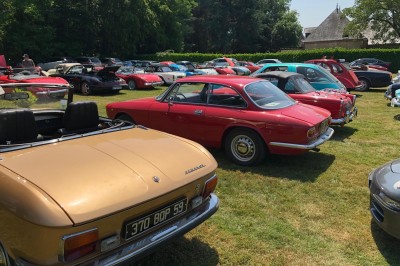 Château en briques rouges entouré de pelouses et d'arbres, sous un ciel clair et ensoleillé.
