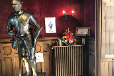 Château en briques rouges entouré de pelouses et d'arbres, sous un ciel clair et ensoleillé.