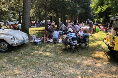 Château en briques rouges entouré de pelouses et d'arbres, sous un ciel clair et ensoleillé.