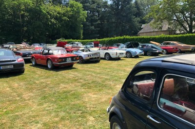 Château en briques rouges entouré de pelouses et d'arbres, sous un ciel clair et ensoleillé.