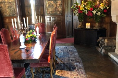 Château en briques rouges entouré de pelouses et d'arbres, sous un ciel clair et ensoleillé.