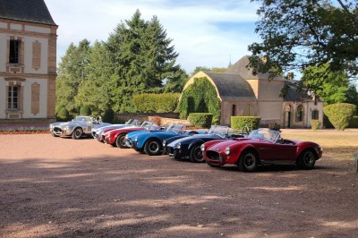 Château en briques rouges entouré de pelouses et d'arbres, sous un ciel clair et ensoleillé.