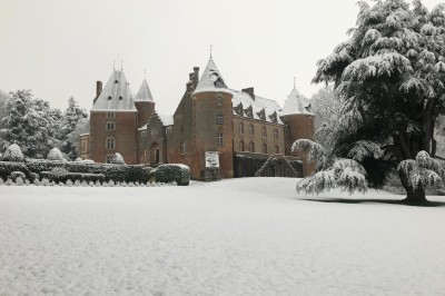 Château en briques rouges entouré de pelouses et d'arbres, sous un ciel clair et ensoleillé.
