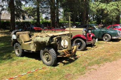 Château en briques rouges entouré de pelouses et d'arbres, sous un ciel clair et ensoleillé.