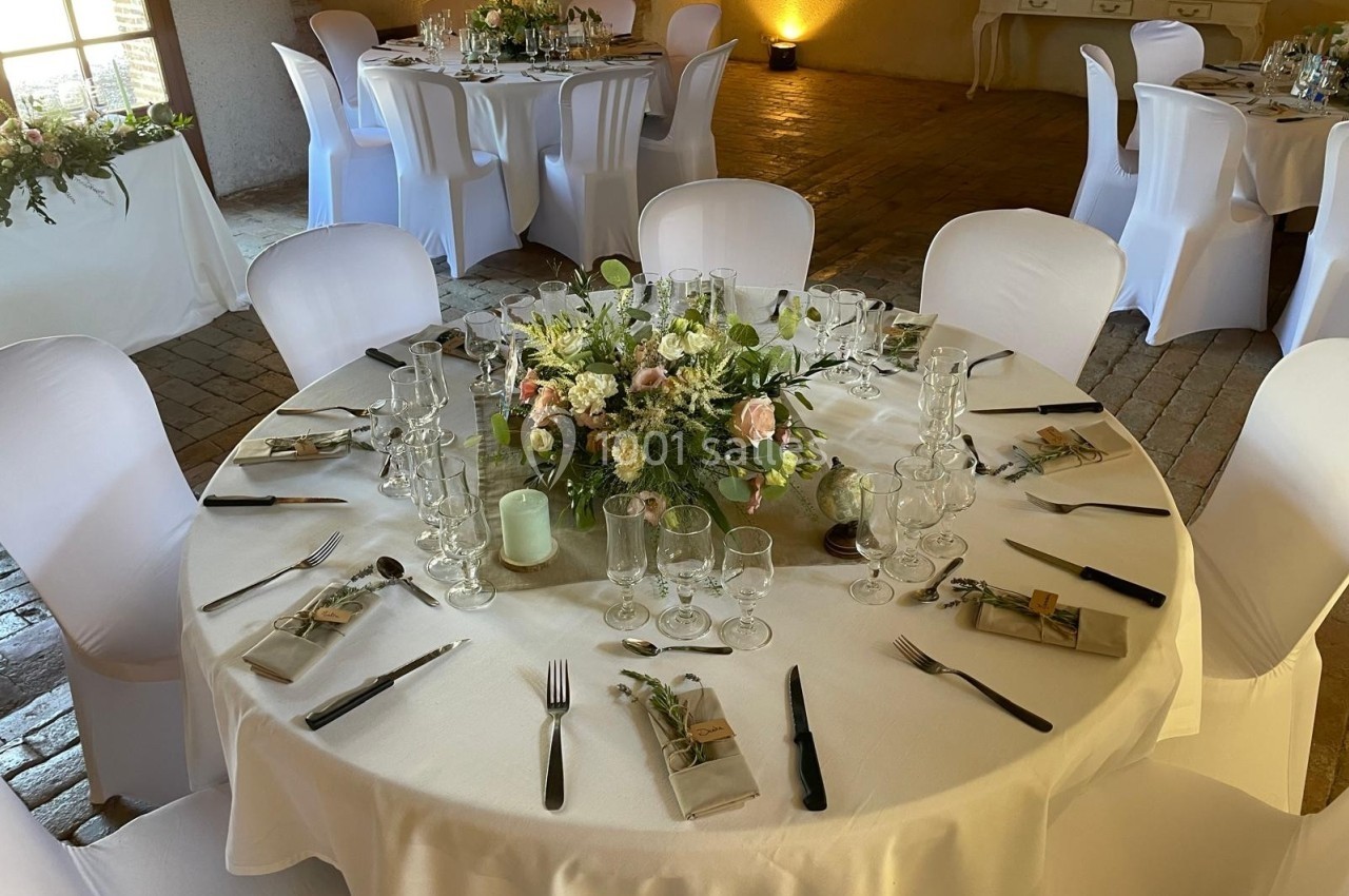 Table ronde élégamment dressée avec une nappe blanche, des couverts, des verres et un centre de table floral.