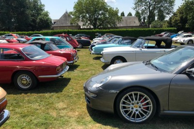 Château en briques rouges entouré de pelouses et d'arbres, sous un ciel clair et ensoleillé.