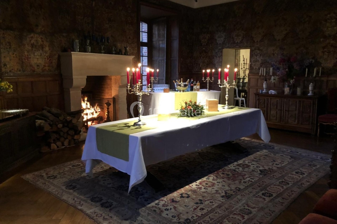 Grande table dressée avec chandeliers et décorations, dans une pièce chaleureuse avec cheminée allumée et tapis au sol.