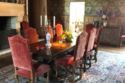 Château en briques rouges entouré de pelouses et d'arbres, sous un ciel clair et ensoleillé.