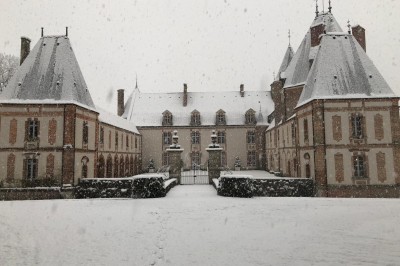 Château en briques rouges entouré de pelouses et d'arbres, sous un ciel clair et ensoleillé.