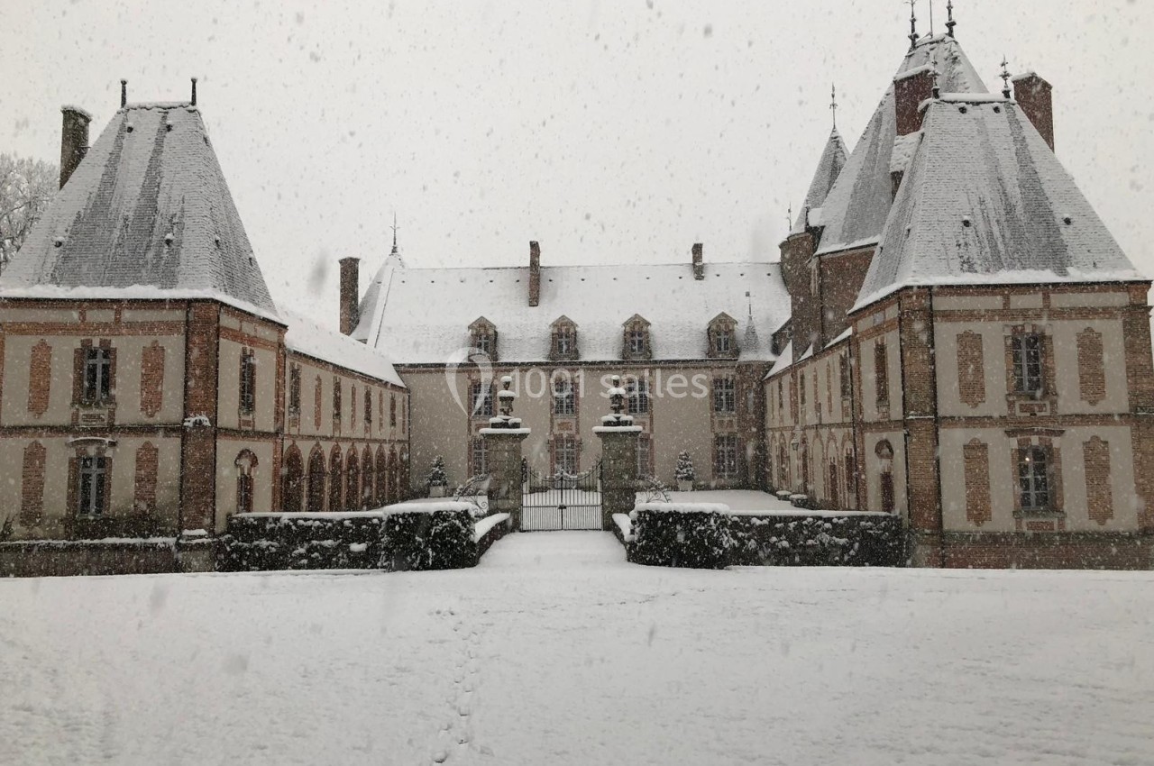 Château entouré de neige sous une forte chute, avec des traces de pas menant à l'entrée principale.