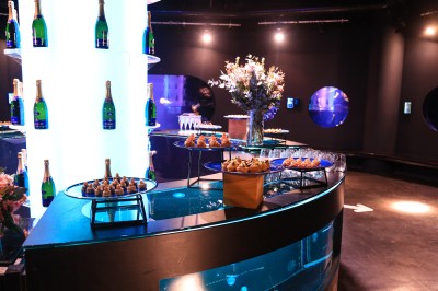 Tunnel d'aquarium avec un grand bassin à droite, éclairages colorés et écran lumineux sur le mur gauche.