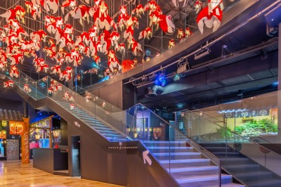 Tunnel d'aquarium avec un grand bassin à droite, éclairages colorés et écran lumineux sur le mur gauche.