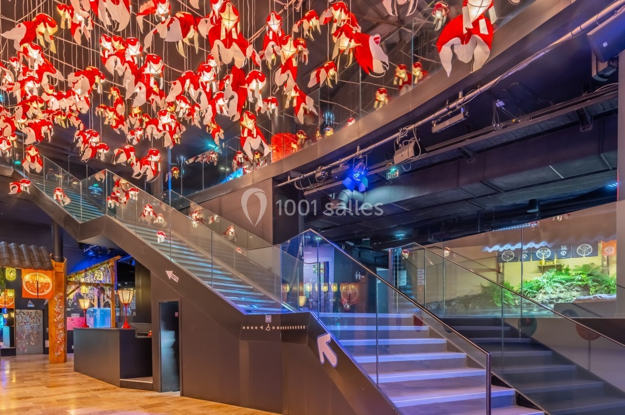 Escalier moderne entouré de décorations suspendues rouges et blanches dans un espace intérieur lumineux.