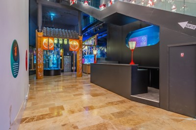 Tunnel d'aquarium avec un grand bassin à droite, éclairages colorés et écran lumineux sur le mur gauche.