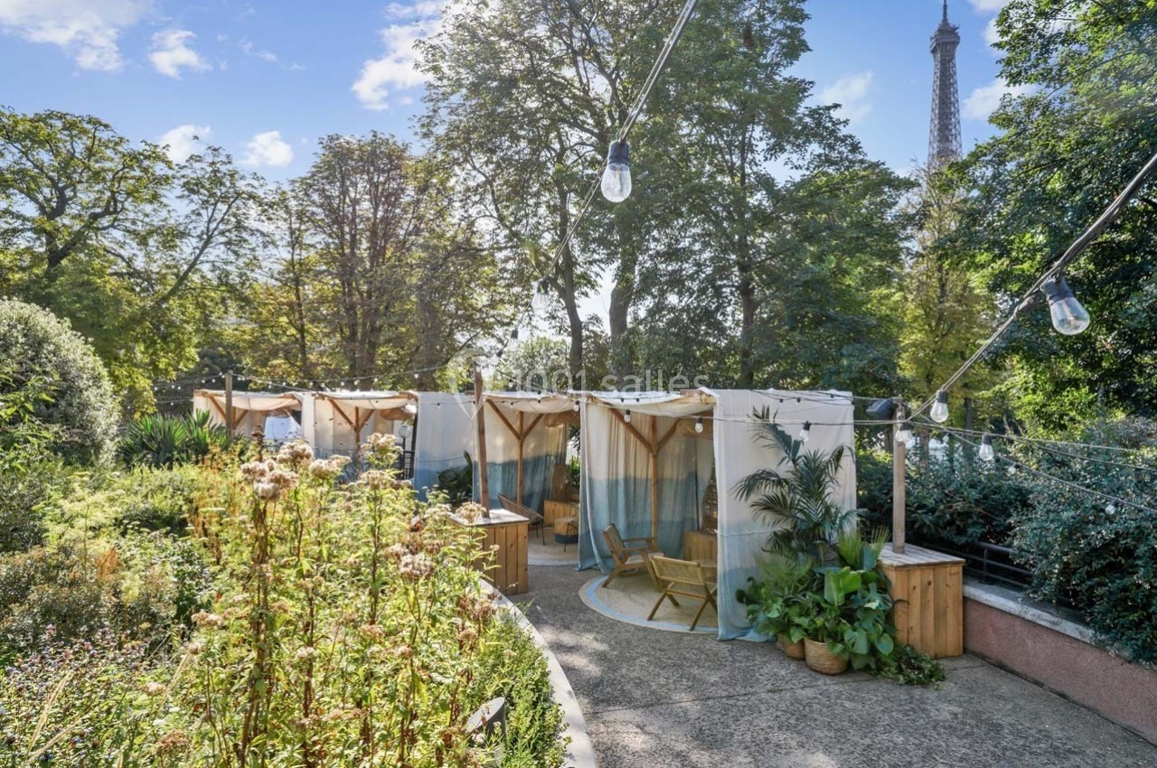 Terrasse aménagée avec des cabines en toile, entourée de végétation, vue sur la tour Eiffel en arrière-plan.