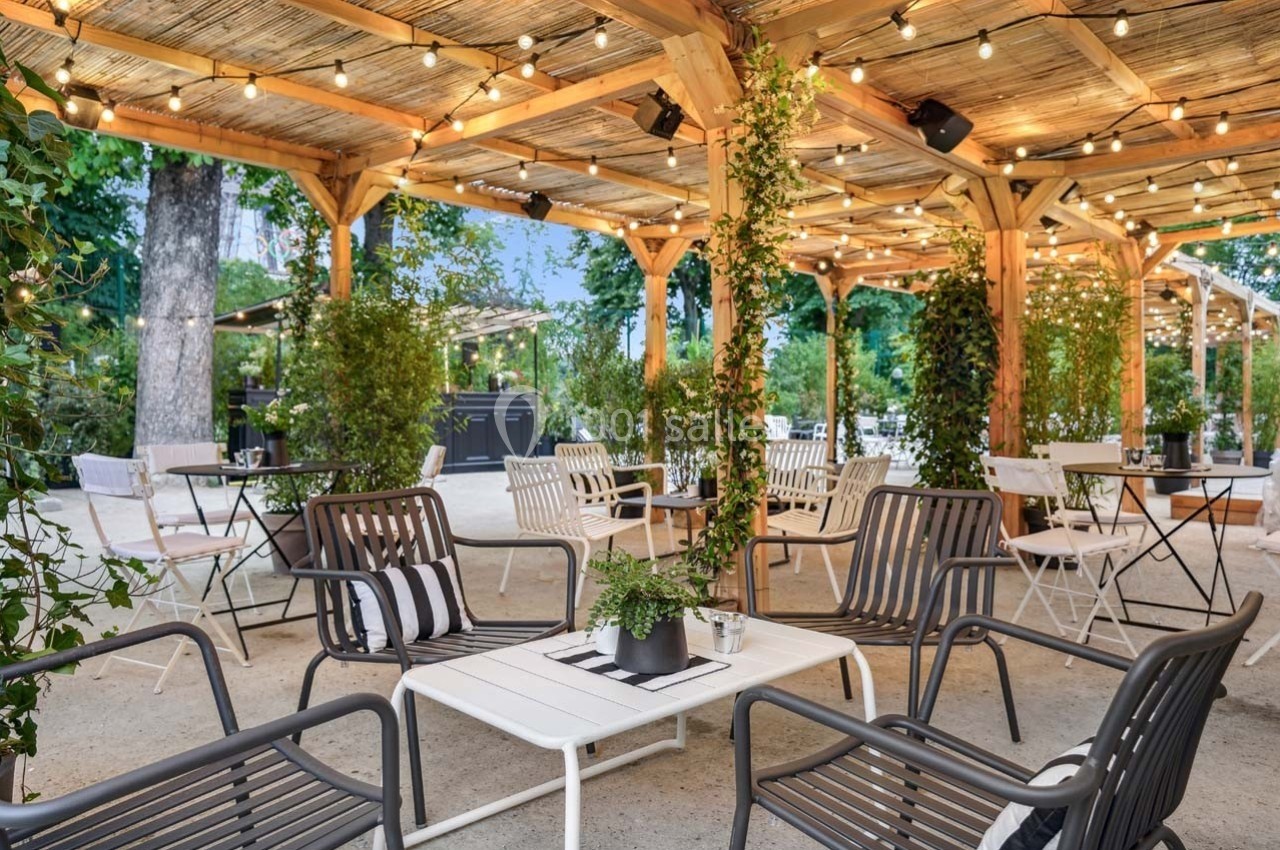 Terrasse extérieure aménagée avec des tables et chaises sous une pergola en bois, éclairée par des guirlandes lumineuses.
