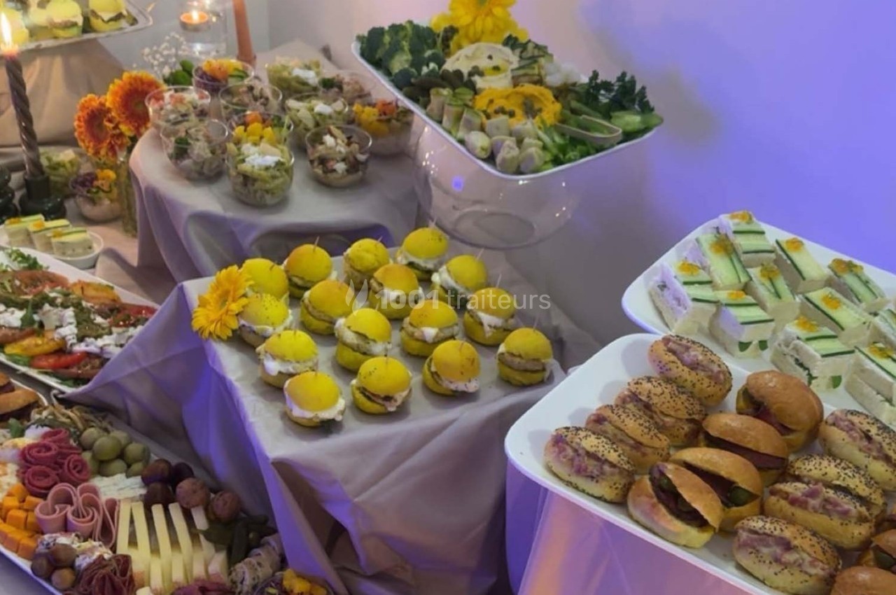 Buffet varié avec sandwichs, salades, fruits, légumes et plateaux de fromages, décoré de fleurs jaunes.