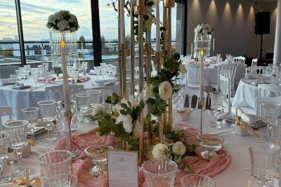 Table de réception élégamment décorée avec chandeliers dorés, fleurs blanches et vaisselle raffinée dans une salle lumineuse.