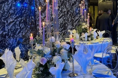 Table élégamment dressée avec chandeliers, fleurs blanches et serviettes pliées, dans une salle au décor sombre et marbré.