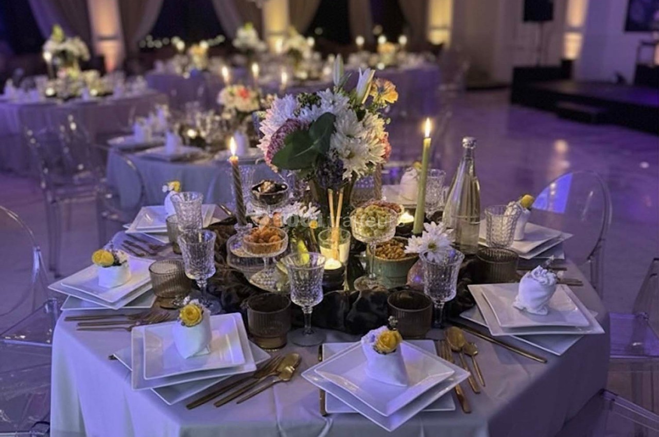 Table élégamment dressée avec vaisselle raffinée, bougies allumées et centre de table floral dans une salle de réception.