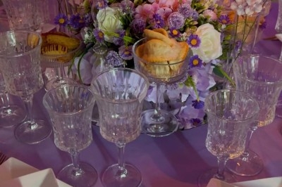 Table de réception élégamment dressée avec chandeliers, fleurs pourpres et vaisselle raffinée dans une salle lumineuse.