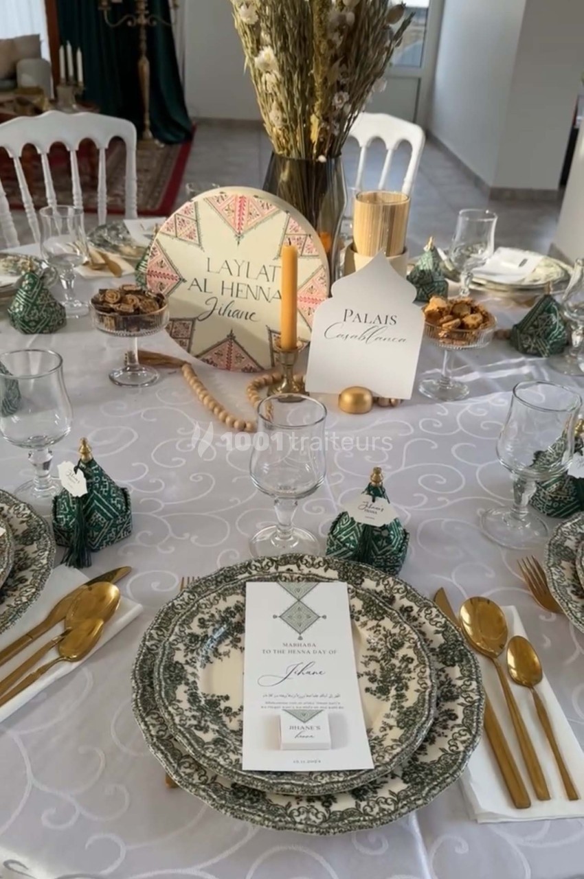 Table élégamment dressée avec vaisselle en porcelaine, couverts dorés, décorations vertes et menu personnalisé.