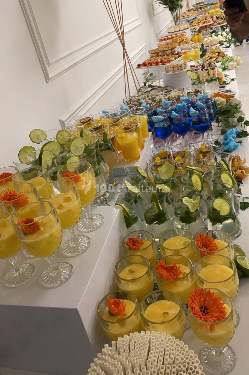 Buffet de boissons colorées disposées sur des tables, avec des verres garnis de fruits et de fleurs.