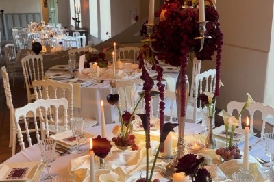 Table de réception élégamment dressée avec chandeliers, fleurs pourpres et vaisselle raffinée dans une salle lumineuse.