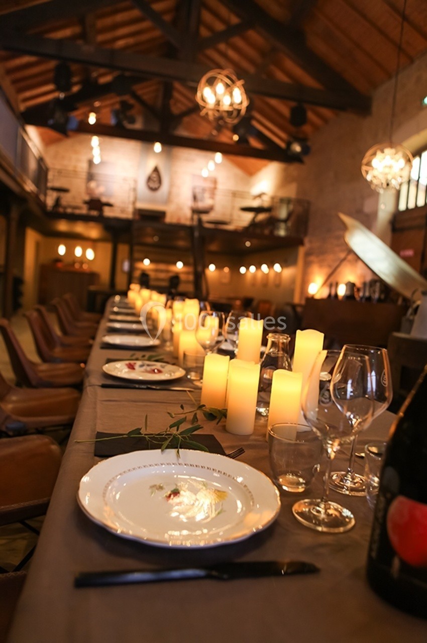 Grande table en bois décorée de bougies et de vaisselle élégante dans une salle aux poutres apparentes et éclairage…