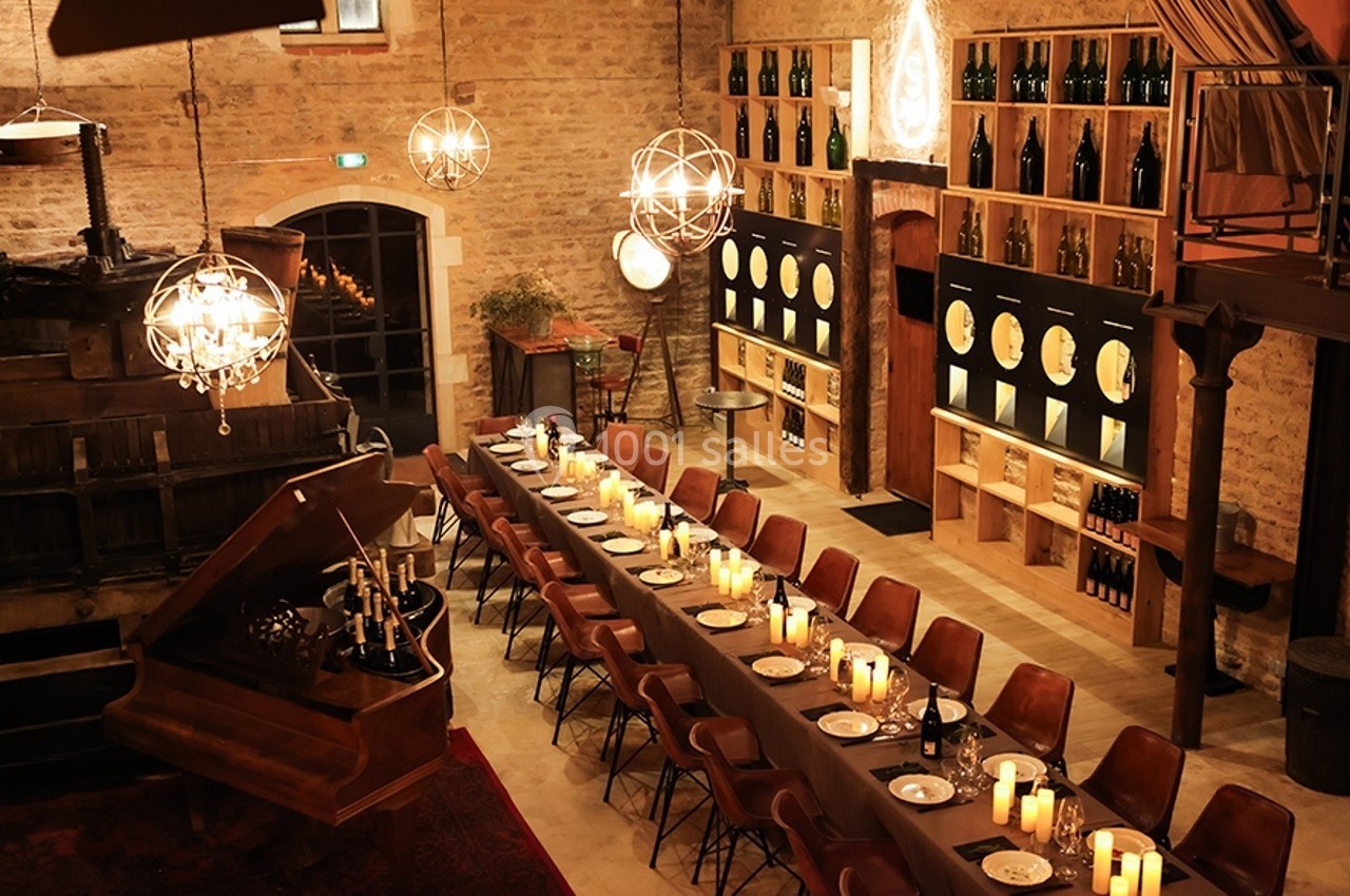 Salle chaleureuse avec une longue table dressée, éclairée par des bougies et des lustres, entourée de murs en pierre et de…
