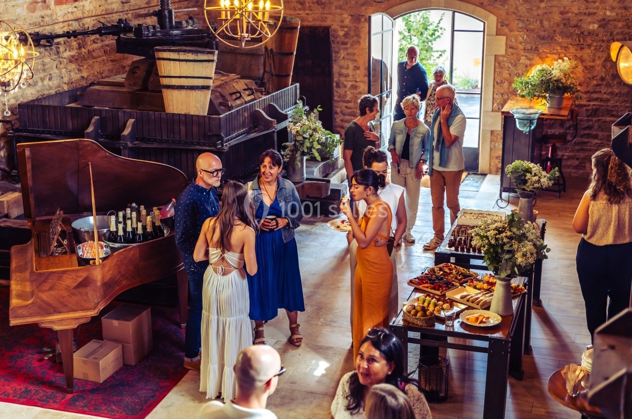 Des invités discutent et dégustent dans une salle chaleureuse avec un piano, des tables garnies et une ambiance conviviale.