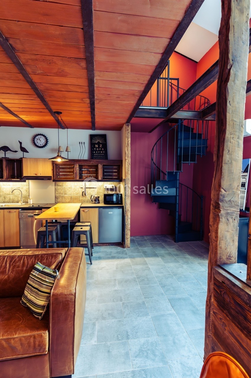 Intérieur d'une maison avec cuisine ouverte, escalier en colimaçon et plafond en bois.