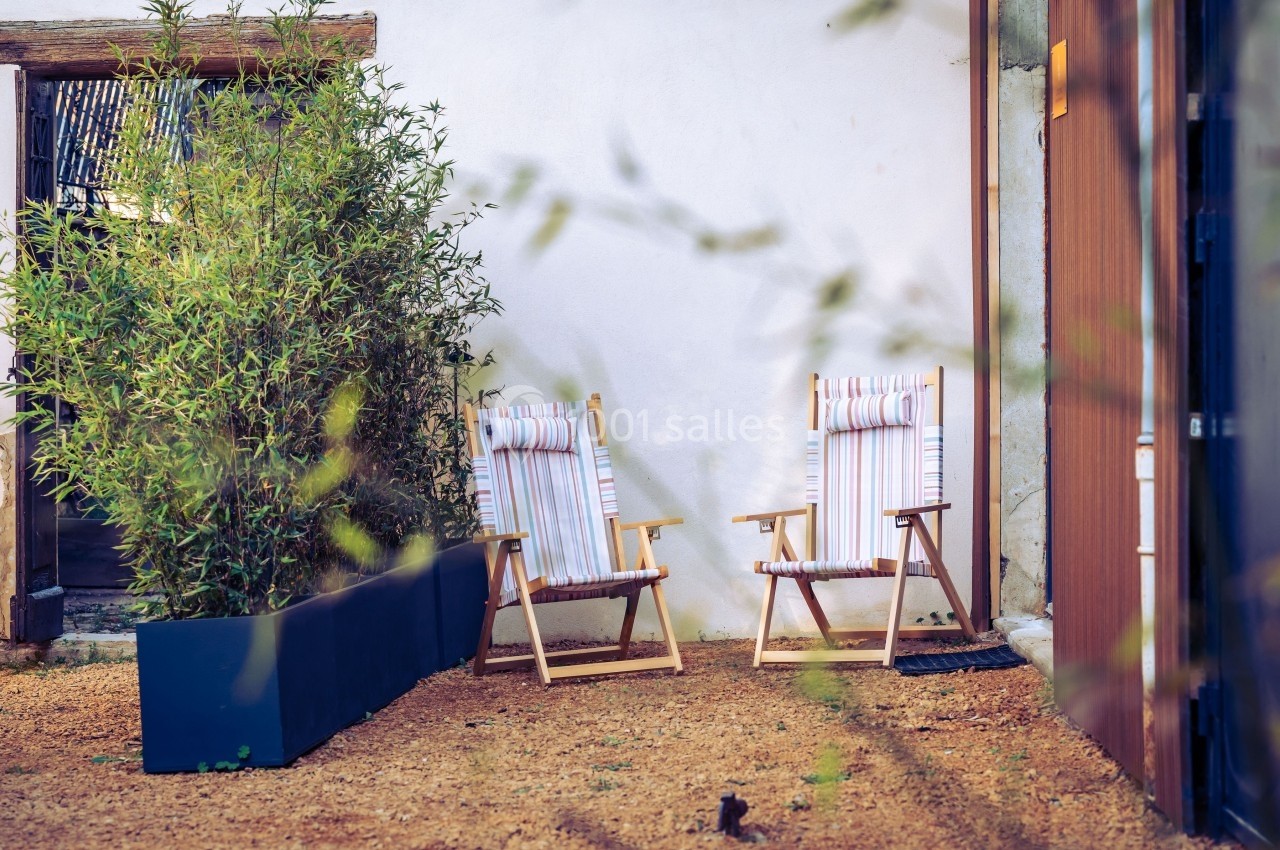 Deux chaises longues à rayures placées sur un sol en gravier, près d'un mur blanc et d'une plante en pot.