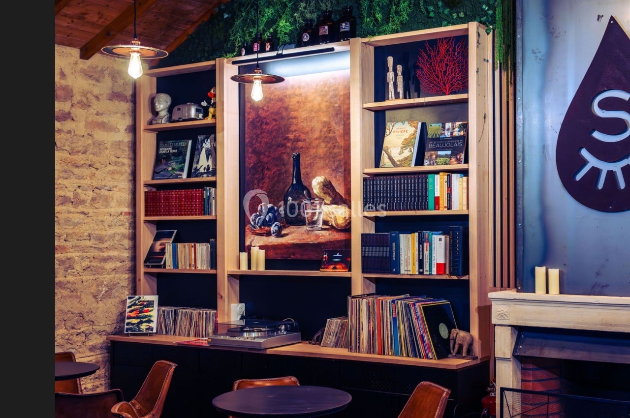 Bibliothèque décorative avec livres, vinyles, objets et tableau nature morte, dans un intérieur chaleureux et éclairé.