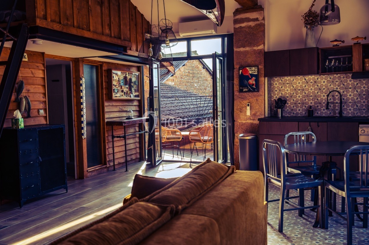 Espace de vie lumineux avec cuisine ouverte, mobilier industriel et accès à une terrasse extérieure ensoleillée.