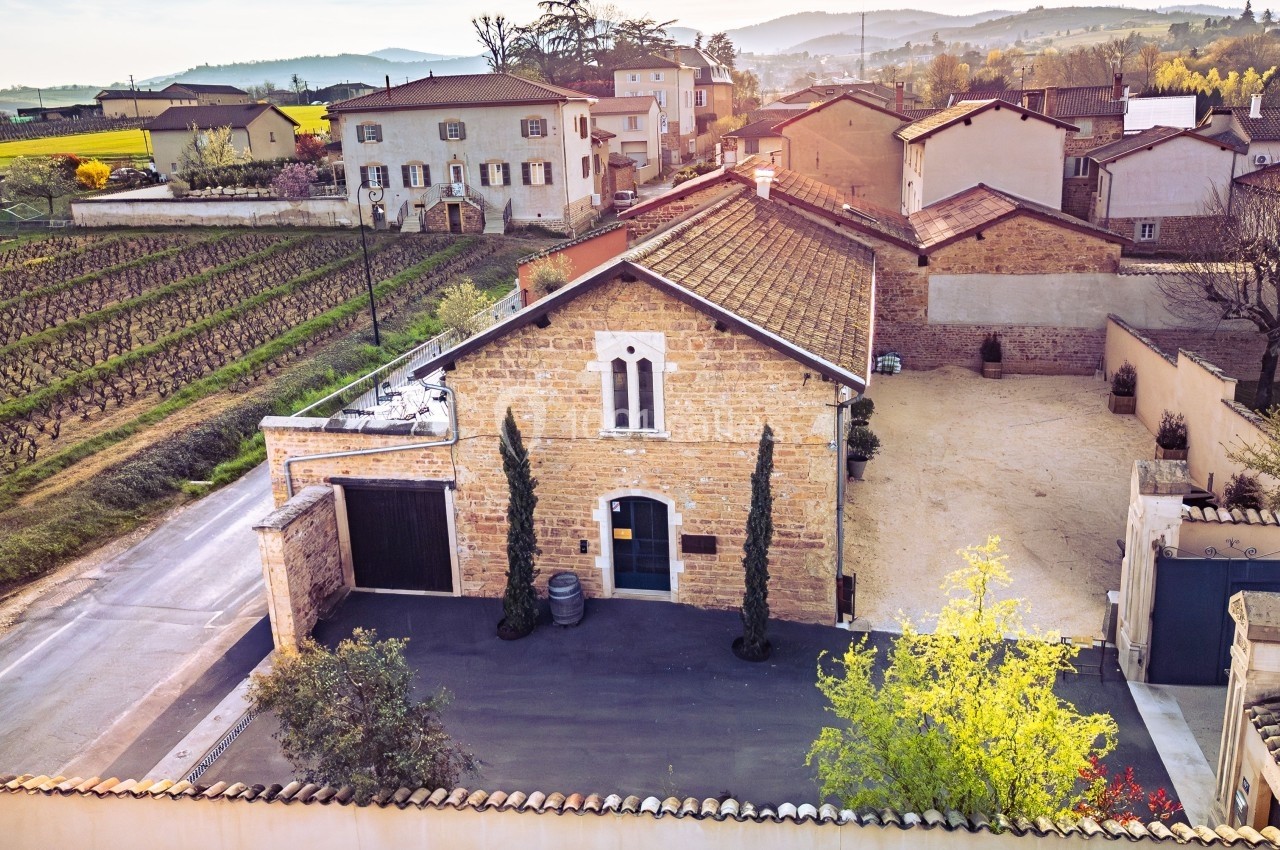 Vue aérienne d'une maison en pierre avec cour pavée, entourée de vignes et de bâtiments dans un paysage rural.