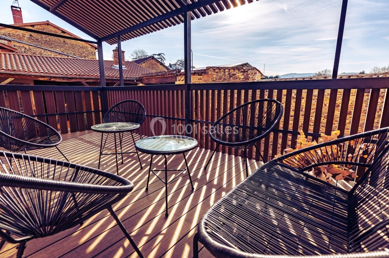 Terrasse en bois avec quatre fauteuils noirs et deux petites tables rondes, entourée d'une balustrade ajourée.