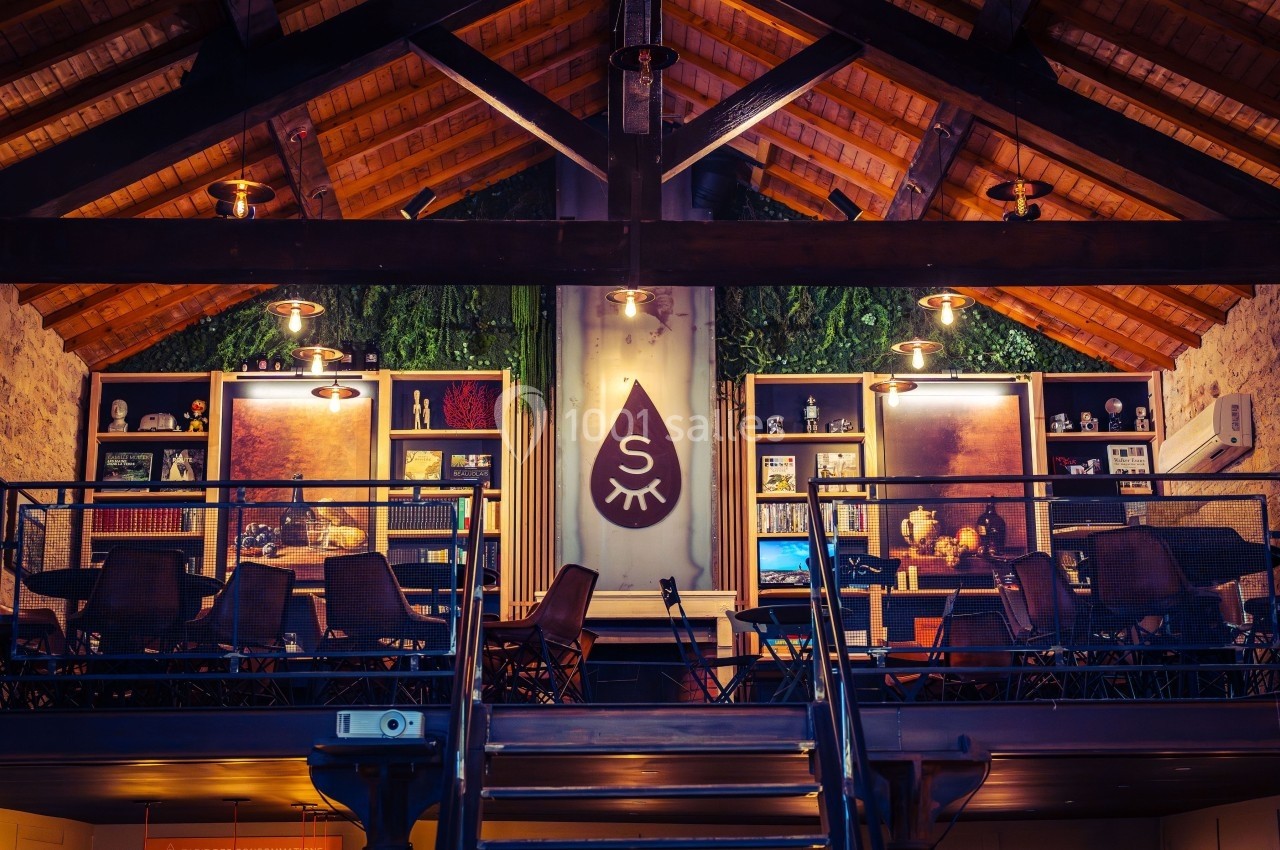 Salle à l'étage avec charpente en bois, éclairage chaleureux, mobilier moderne et décoration végétale.