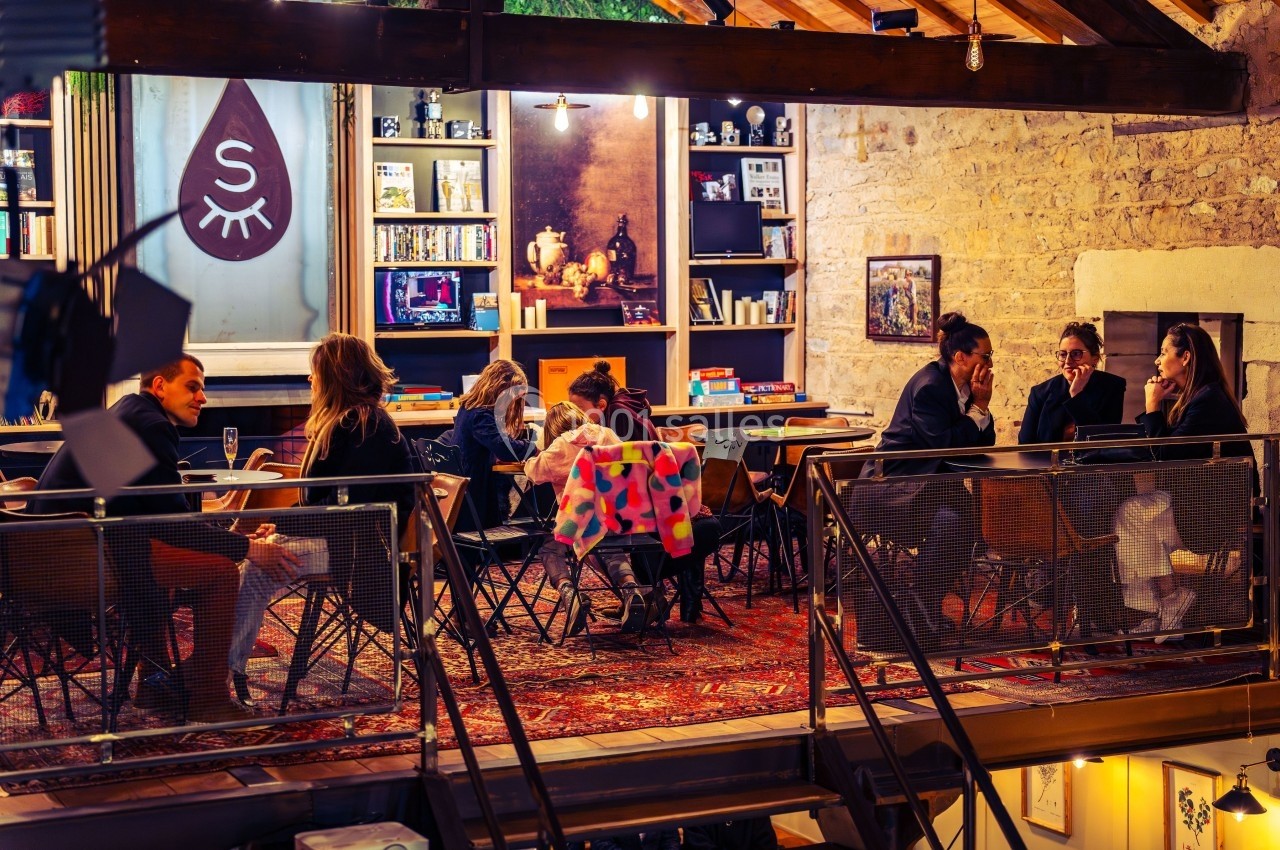 Des personnes discutent autour de tables dans un espace chaleureux avec des étagères et une décoration éclectique.